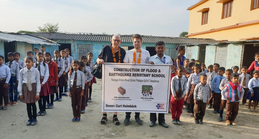 Curt, Björn Söderberg och skolans rektor visar upp skylten som förkunnar att det ska byggas en ny skola, allt medan skolbarnen högtidligt ställt upp sig på den provisoriska skolgården.