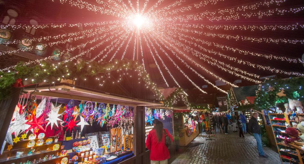 Festliga julstjärnor och smyckade granar bjuder in till en mysig promenad genom den traditionella julmarknaden runt torget i Lübeck