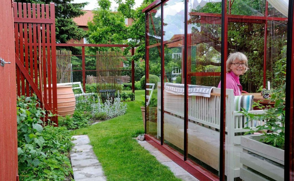 Det röda växthuset är hjärtat i trädgården Christina tillbringar mycket tid. Den röda färgen går igen i bodar och staket. Foto: Ellen Forsström