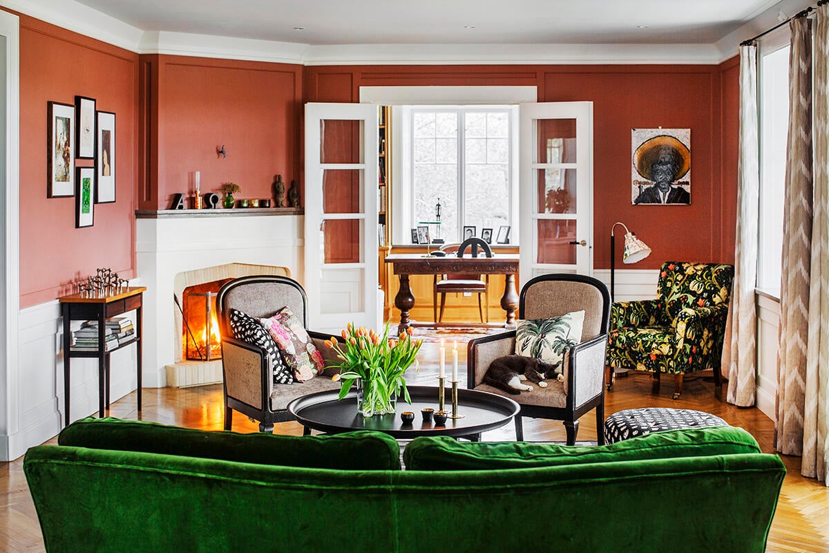 Vardagsrummet med en välvd, grön sammetssoffa, omklädda fåtöljer och ett rymligt brickbord ger ett mysigt intryck. Man kan förstå att katten Zelda har sin favoritplats här. Foto: Lina Östling