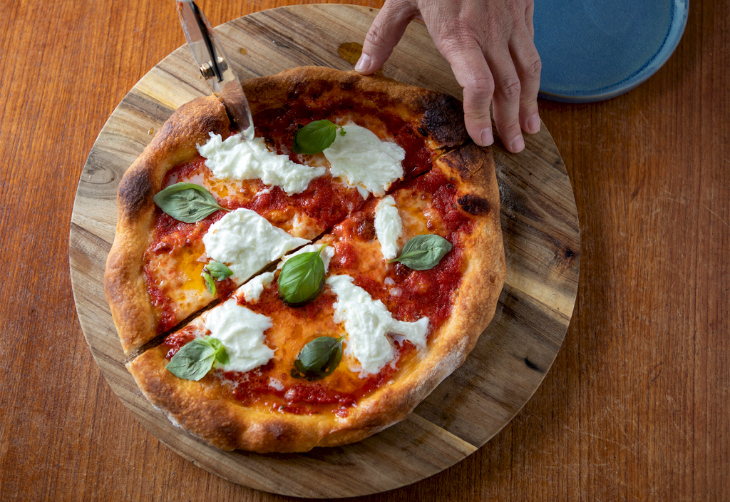 Pizza margherita delas med pizzadelare. 