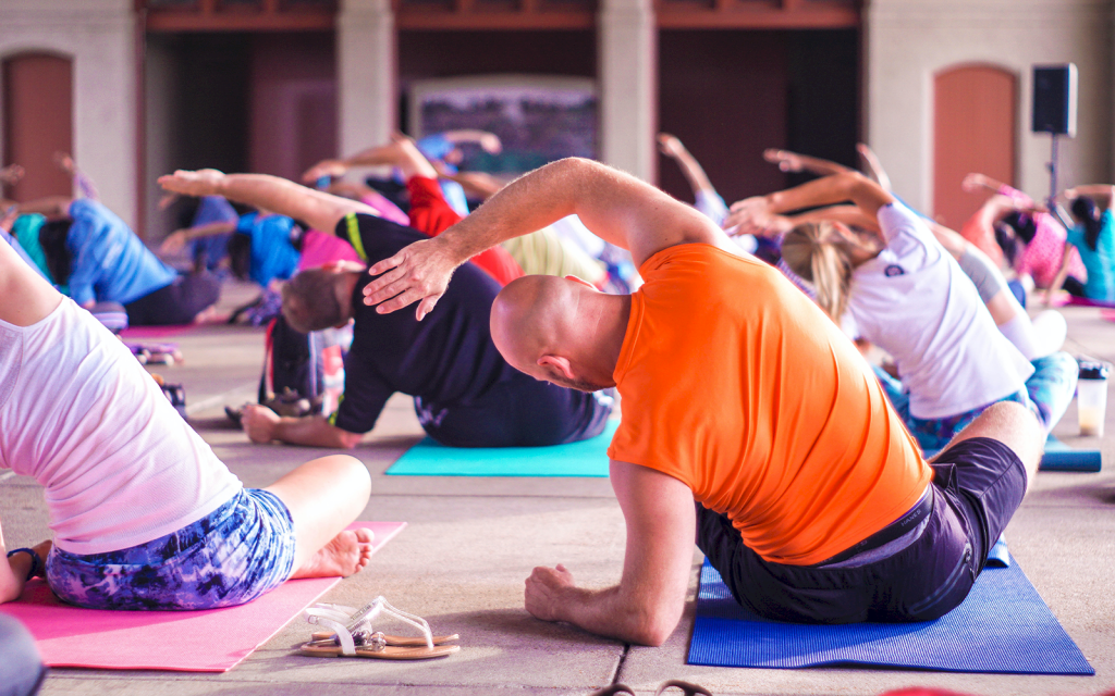 Personer på yogaklass sitter på yogamattor och lutar sig åt sidan.