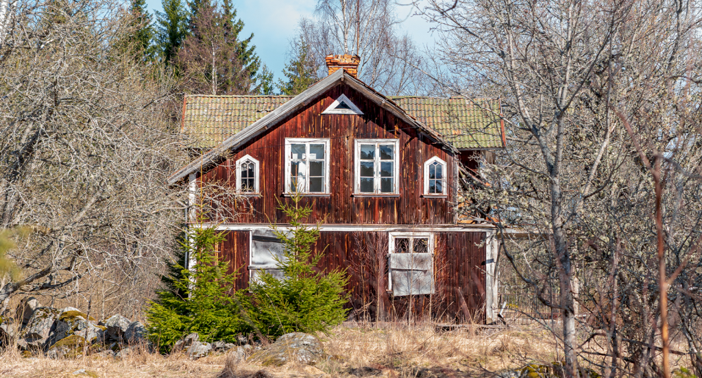 Ett rött hus på landet som ser ut att vara i behov av renovering.