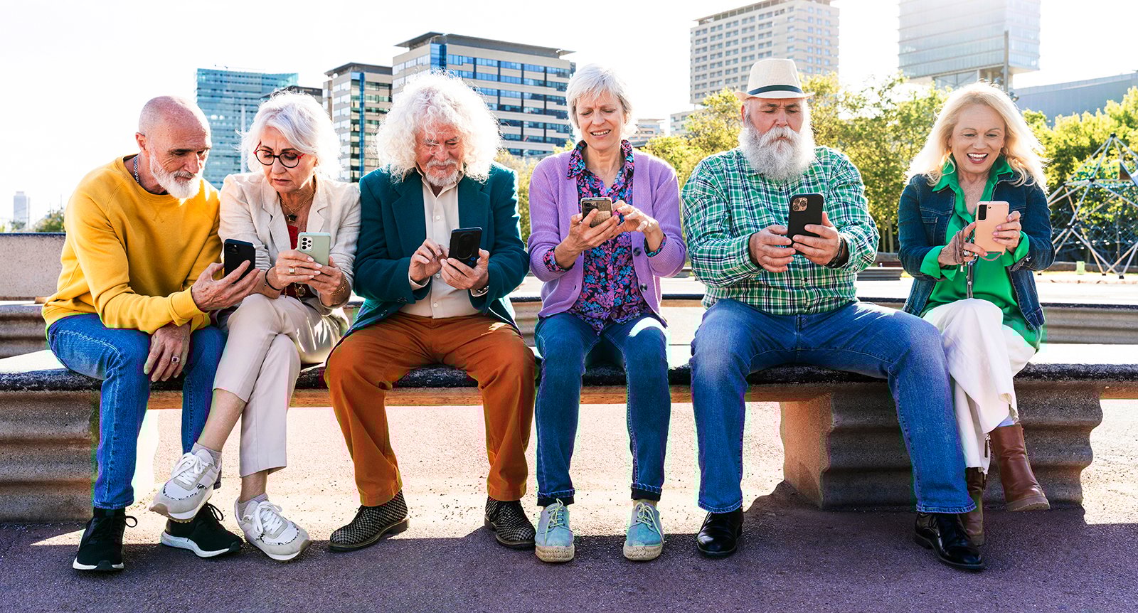 Äldre vänner sitter på bänk och använder mobiltelefoner.