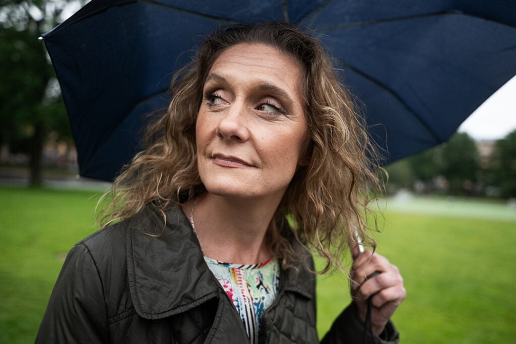 Porträttbild på skådespelaren Kateryna Kisten, en kvinna i brunt, lockigt hår som håller i ett paraply.